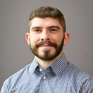 man with dark hair and bear wearing a checkered dress shirt