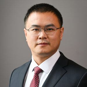 man with short hair wearing glasses, dark suit, white shirt and red tie