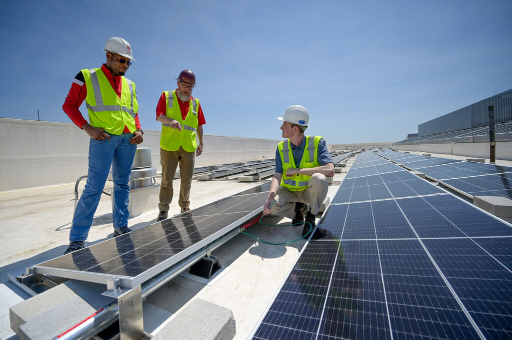 Shane Fogarty, right, a student intern working as construction project manager, takes a look at solar panels installed on the Fitts-Woolard Engineering building on Centennial Campus with Jim Rains, construction manager, center, and Raheem Ariwoola, energy engineer, left.