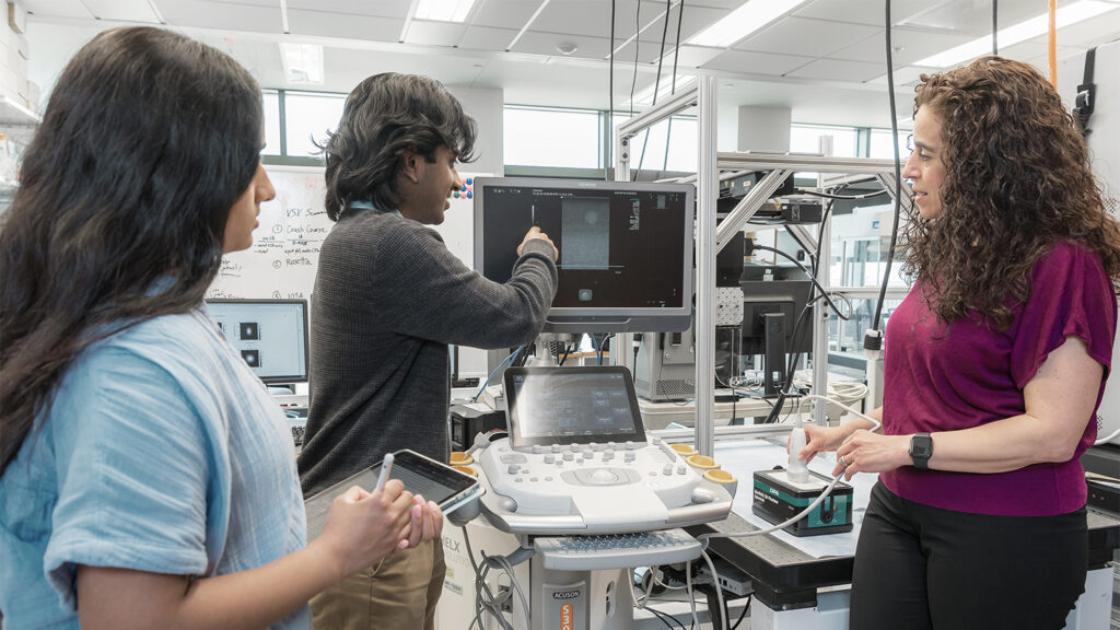 Three students look at a computer screen in a NCSU UNC joint biomedical lab.