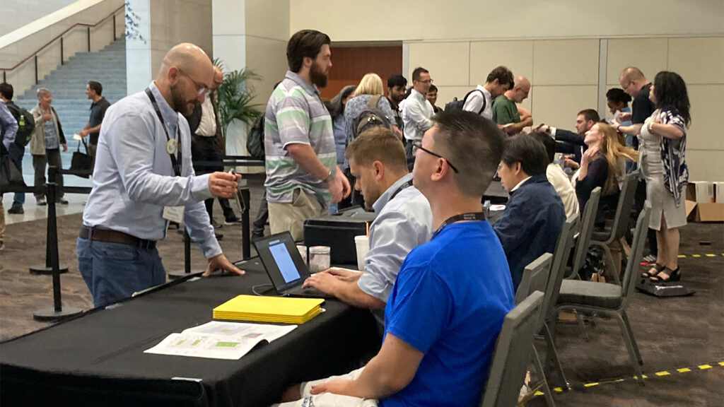 Photo from the International Soft Matter Conference 2024 showing attendees on the left checking in at a table on the right covered by a black table cloth and staffed by several seated people 