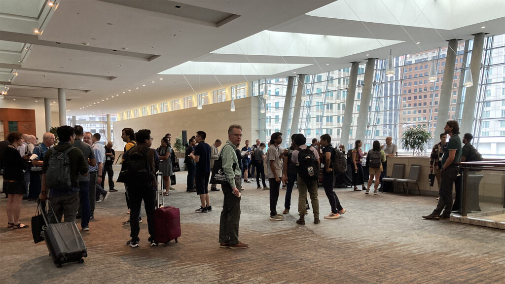 Photo from the International Soft Matter Conference 2024 showing a large group of attendees in a large open area with floor to ceiling windows.