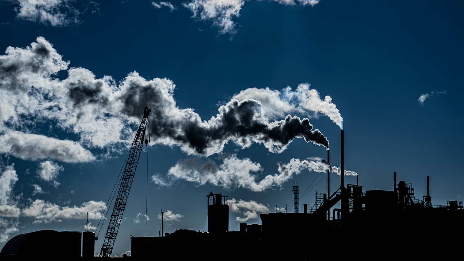 factory smokestacks spew smoke against the backdrop of a blue sky