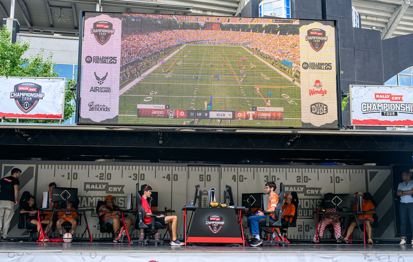 Two gamers compete beneath a large video display of their game.