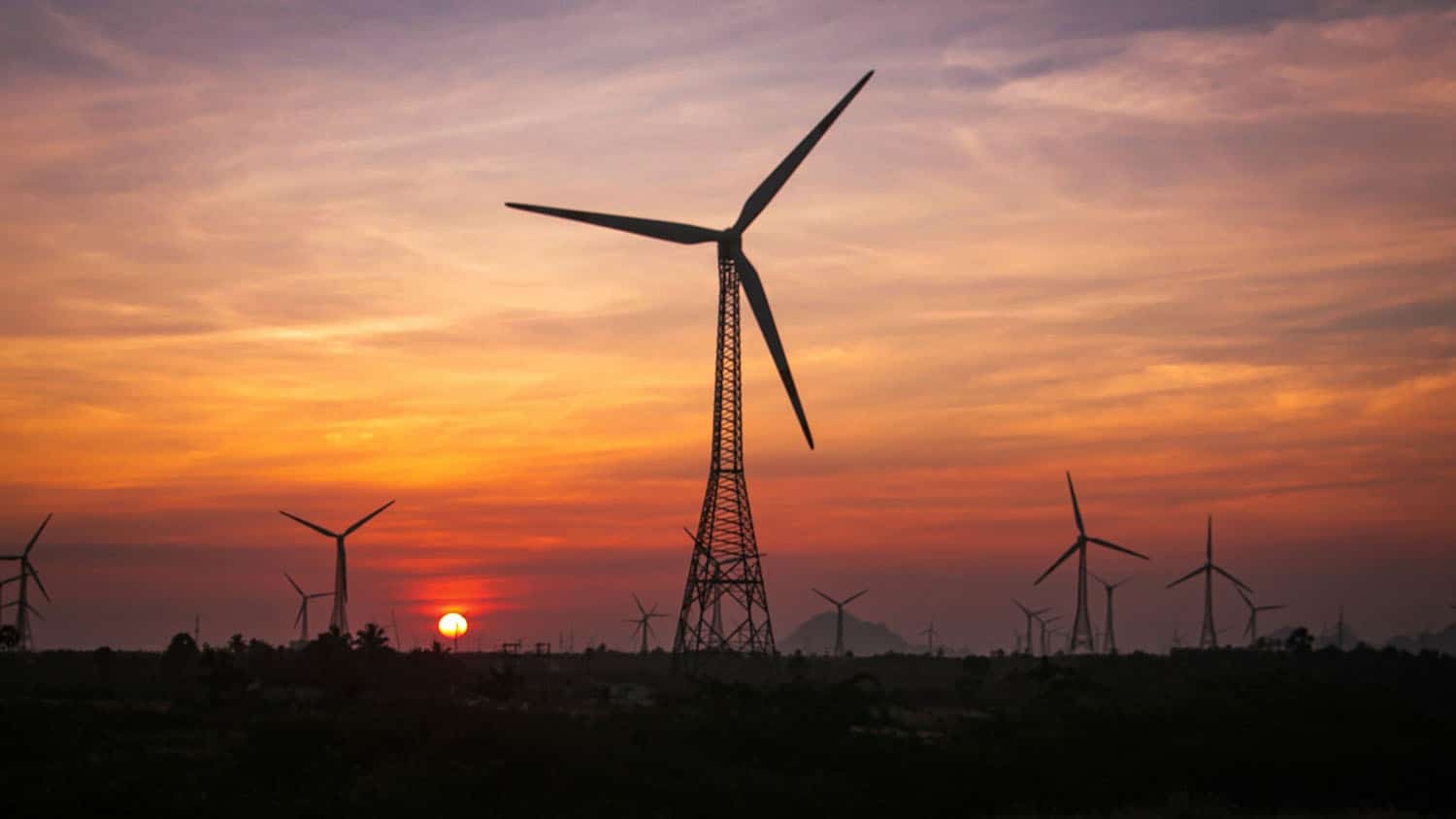 a row of windmills is silhouetted against a sunrise