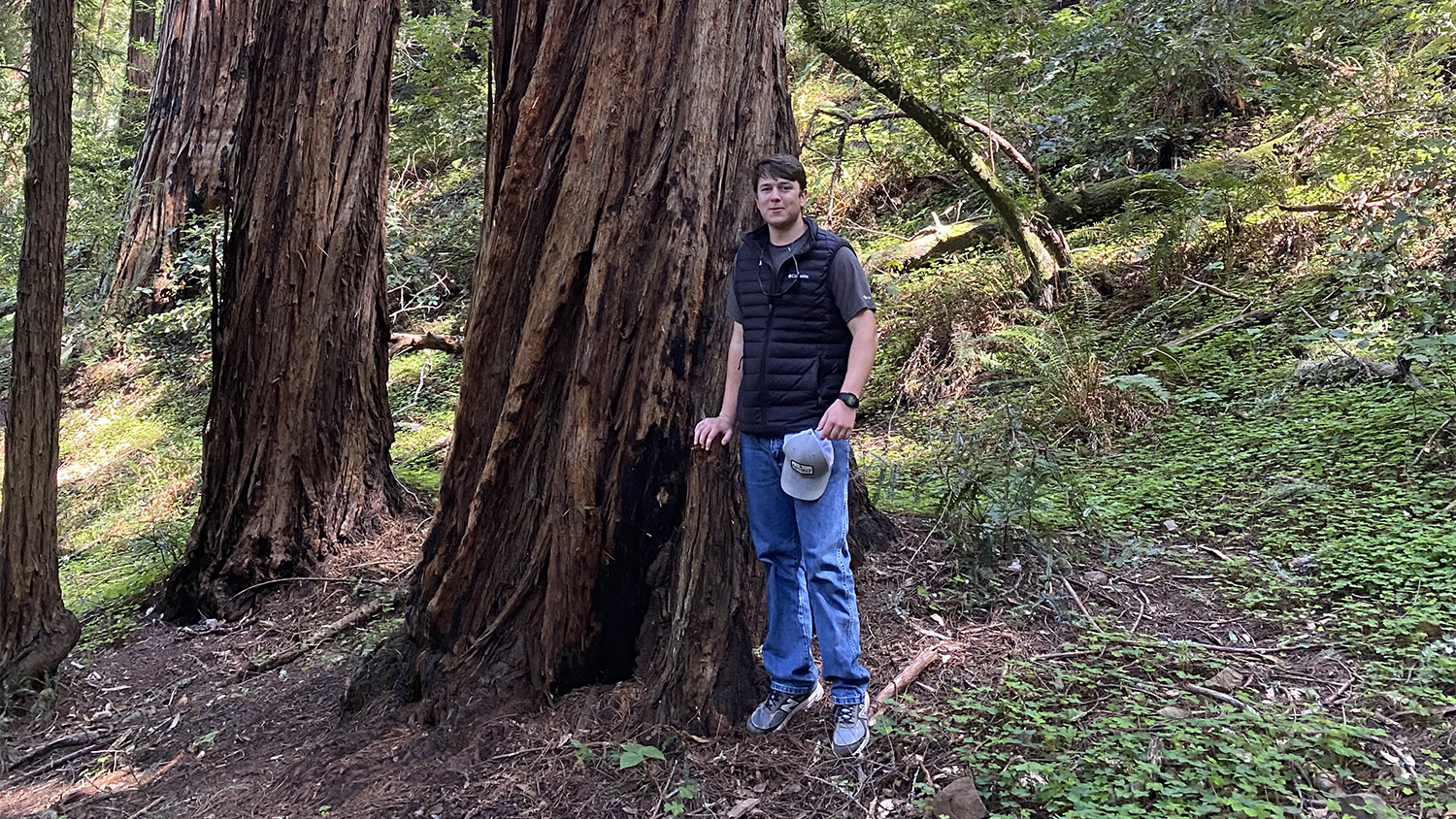 Camerson Stephenson stands next to a large tree in a forest.