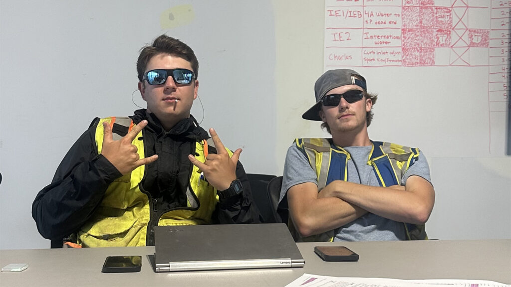 Cameron Stephenson, left, and friend sitting at a table wearing sunglasses and high-visibility jackets.