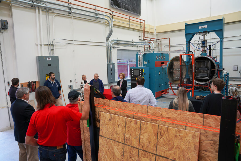 Afsaneh Rabiei, center background, speaks to a group assembled in the newly opened Hot Press Furnace facility.