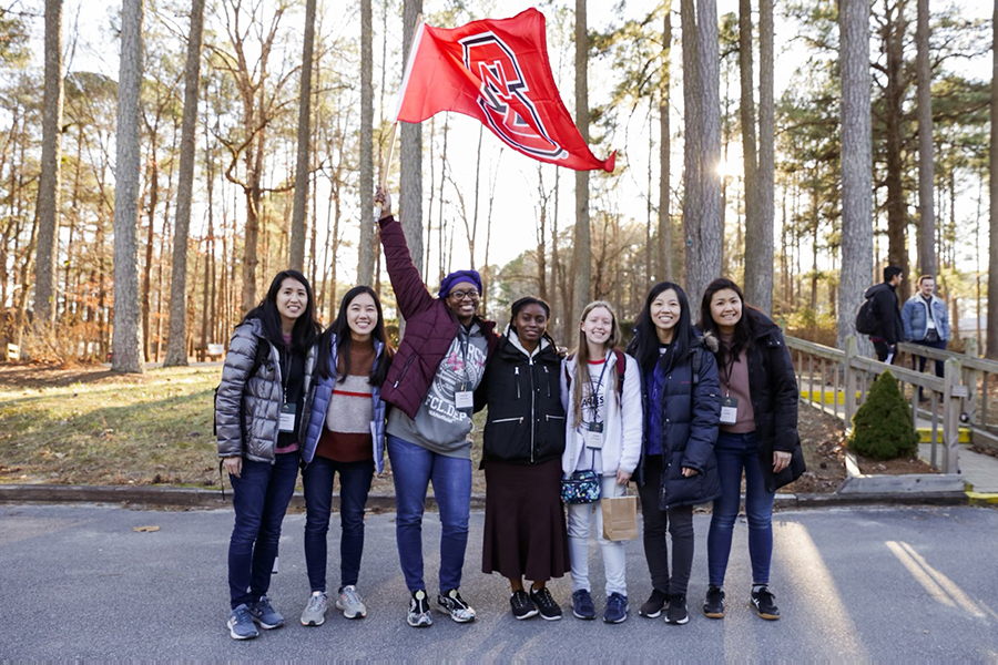 Tabitha Gardner, third from left, raises the NC State flag while posing for a group photo with friends.