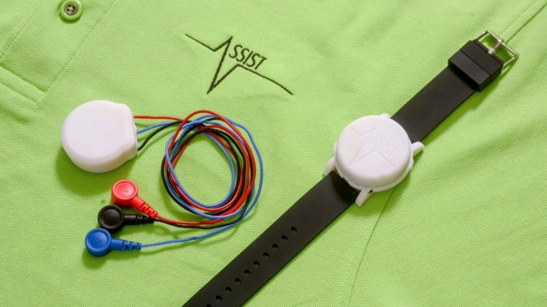 A set of red, black and blue sensors and a black and white watch rest on top of a lime green knit shirt with the ASSIST logo embroidered on it.