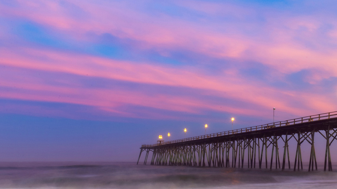 Pier at Kure Beach at sunset. Clouds are deep blue and pink.