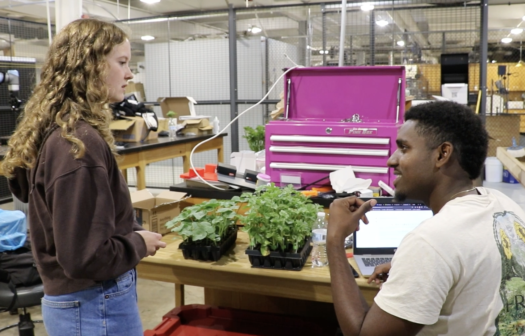 Two students in a lab tend to young plants at a work table.