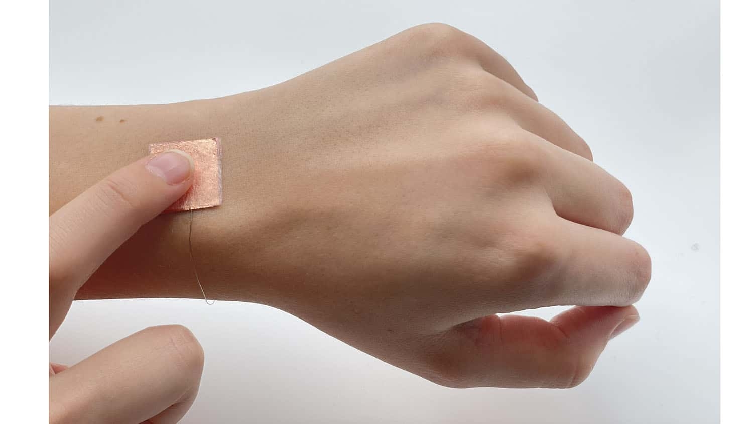 a small patch rests on the back of a person's left wrist. the person is touching the patch with their right index finger