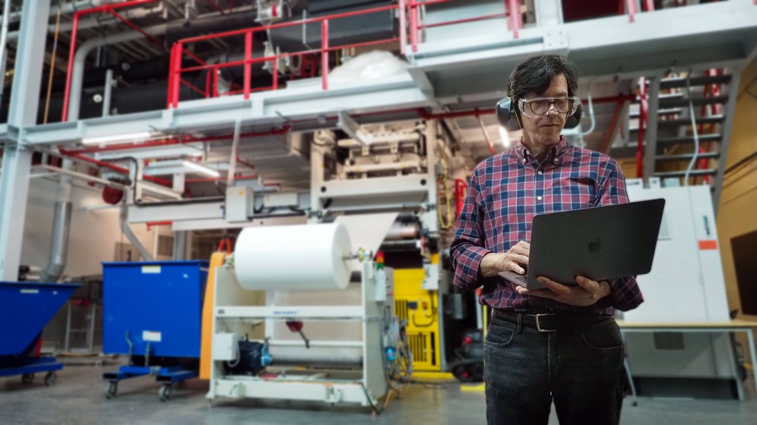 A worker with a laptop monitoring the performance of an integrated manufacturing system