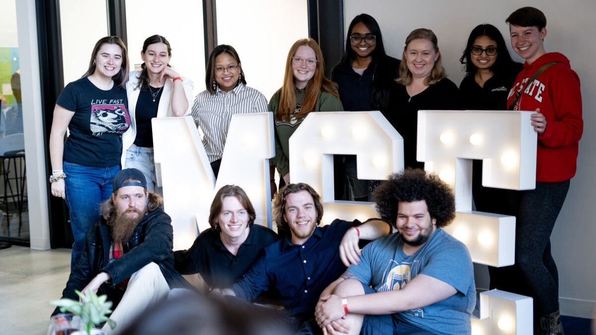 Undergraduate students pose for a group picture around an illuminated MSE sign.