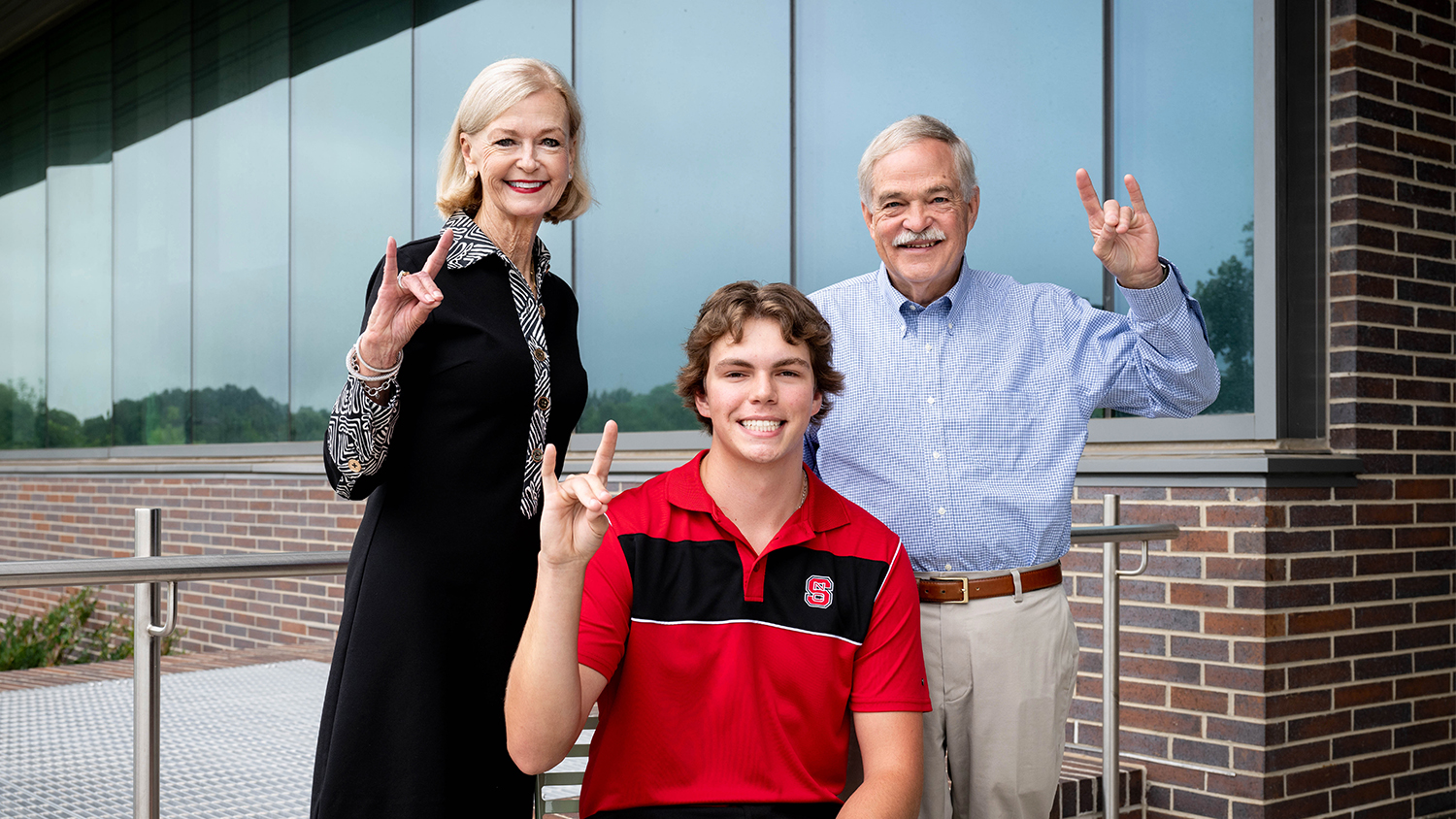Barbara Pleasant, left, and Dan Pleasant, right, show the NC State wolf sign along with Braydon Boaz, middle.