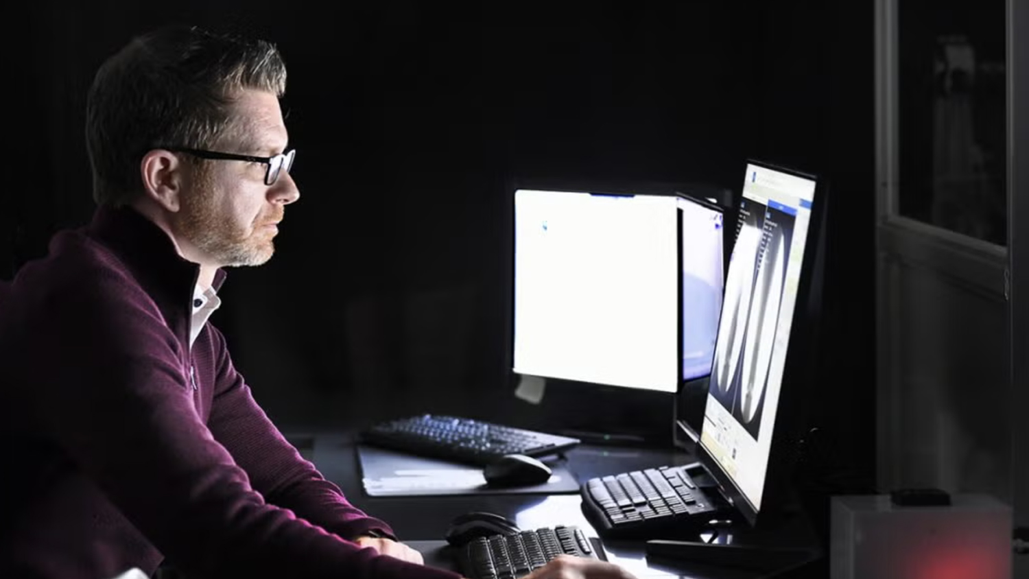 Jason Franz, left, sits in front of multiple computer screens in a dark room.
