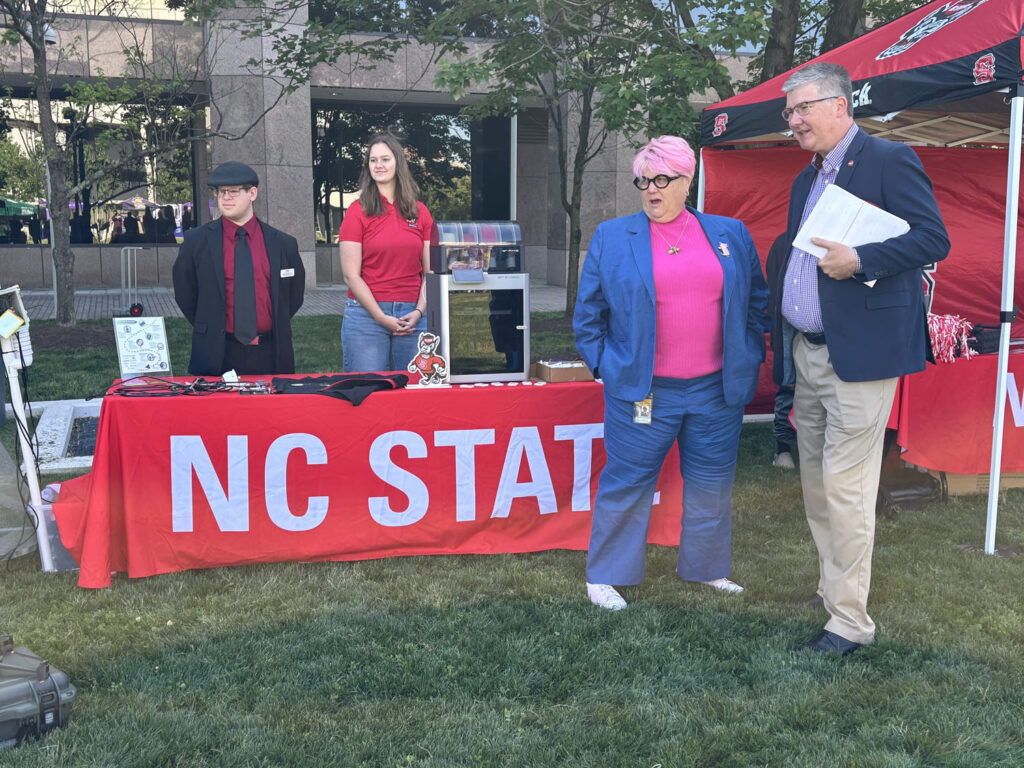 Attendees look to the left while talking in front of a large NC State red table banner