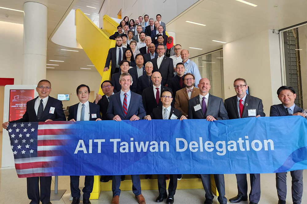 Taiwan delegation group photo at Hunt Library. Group is assembled on large yellow staircase leading from the second floor to the first floor. The front row holds a banner reading "AIT Taiwan Delegation" in white letters on a blue background.