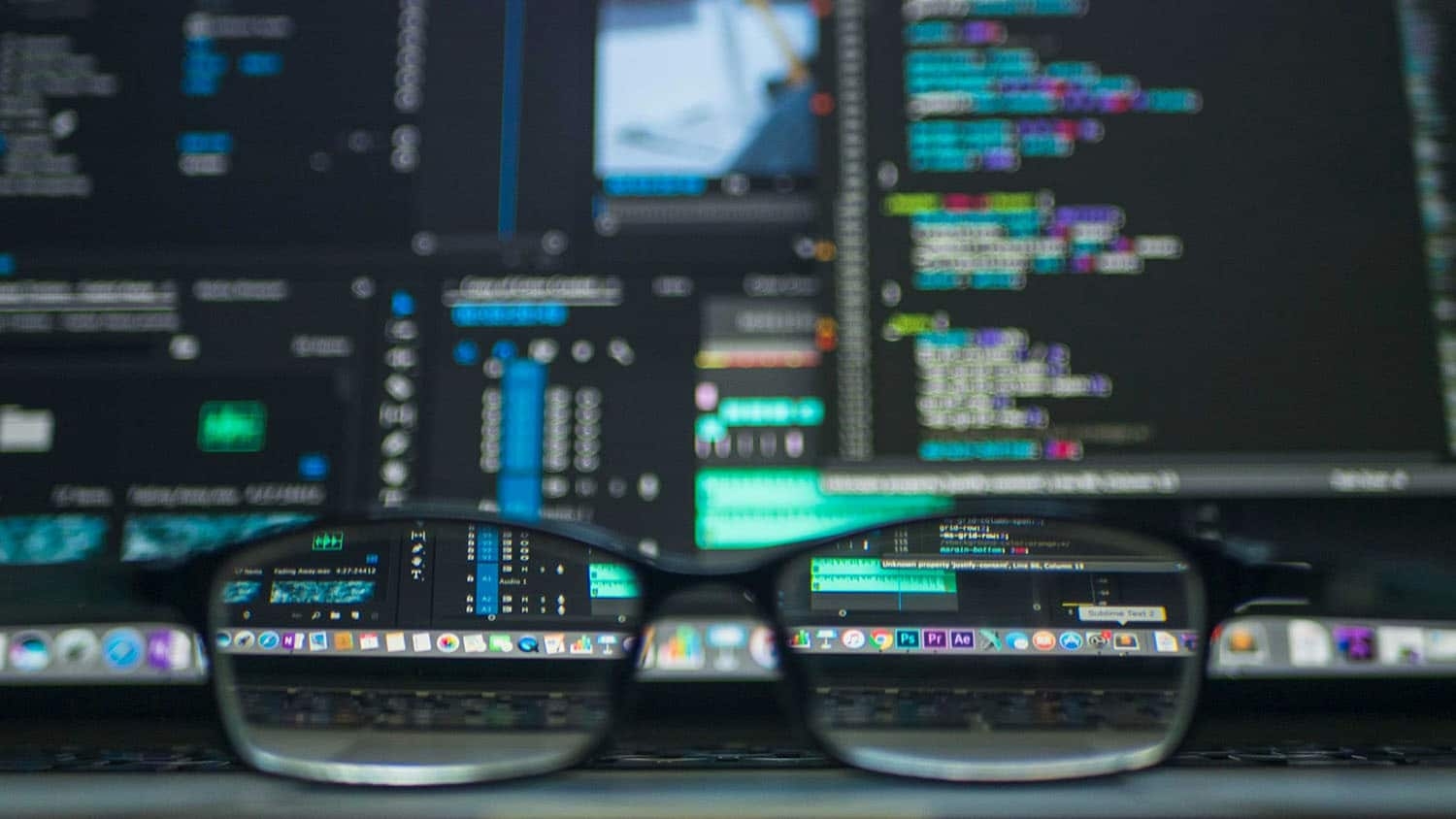 a pair of eyeglasses rests on a desk in front of a computer screen that is running code