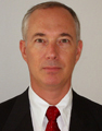 older man wearing a dark suit, white dress shirt and red necktie