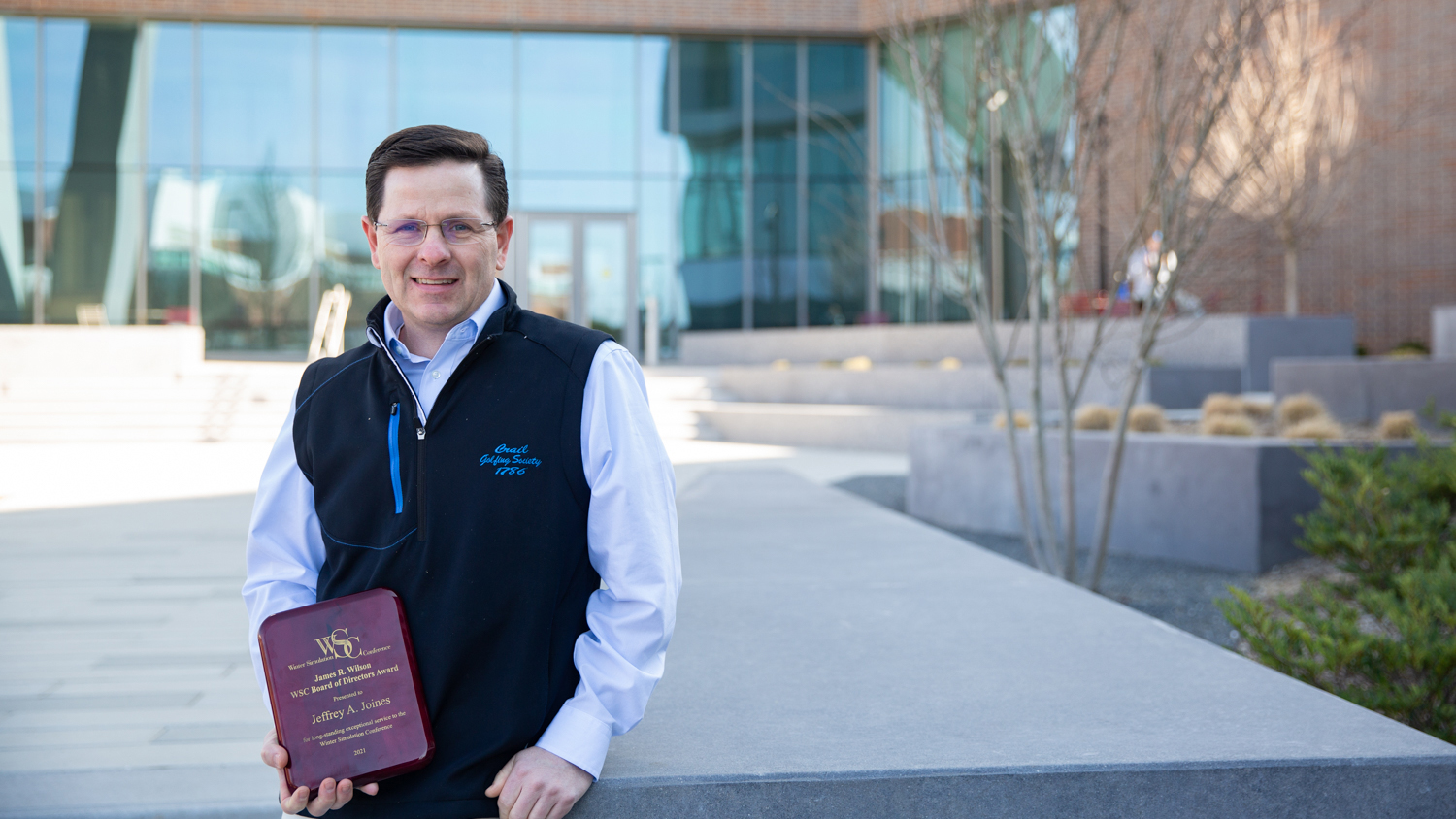 Jeff Joines standing outside holding a book in front of entrance to Fitts-Woolard Hall.