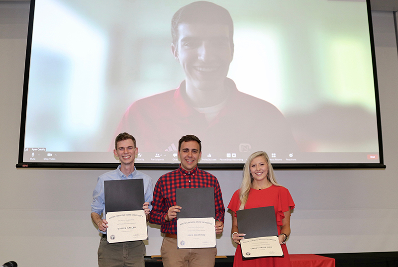 Four winners pose for picture, three in person, one on-screen.