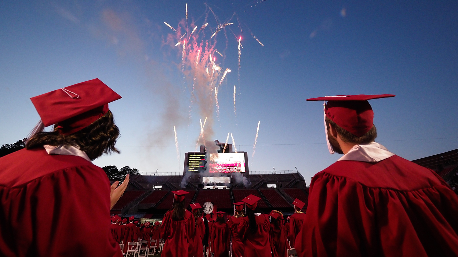 Graduates in regalia watch fireworks at Carter-Finley Stadium.