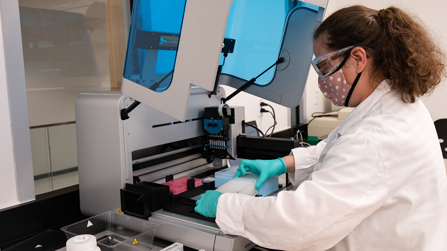 Masked and gloved researcher conducts tests in environmental lab.