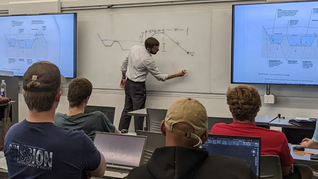 Charles Townsend writes on dry erase board at front of classroom while guest lecturing.