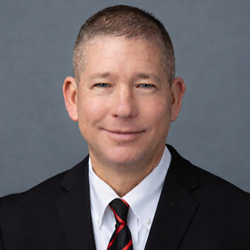 man with short cropped hair wearing a white dress shirt, dark jacket and red and black striped necktie