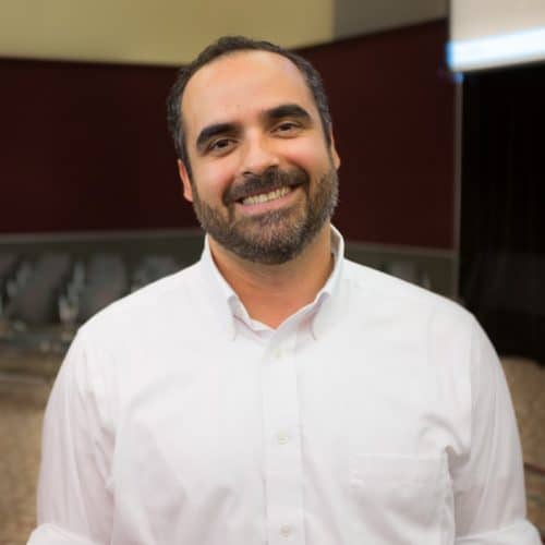 older man with short dark hair, short beard, wearing a white button-up shirt