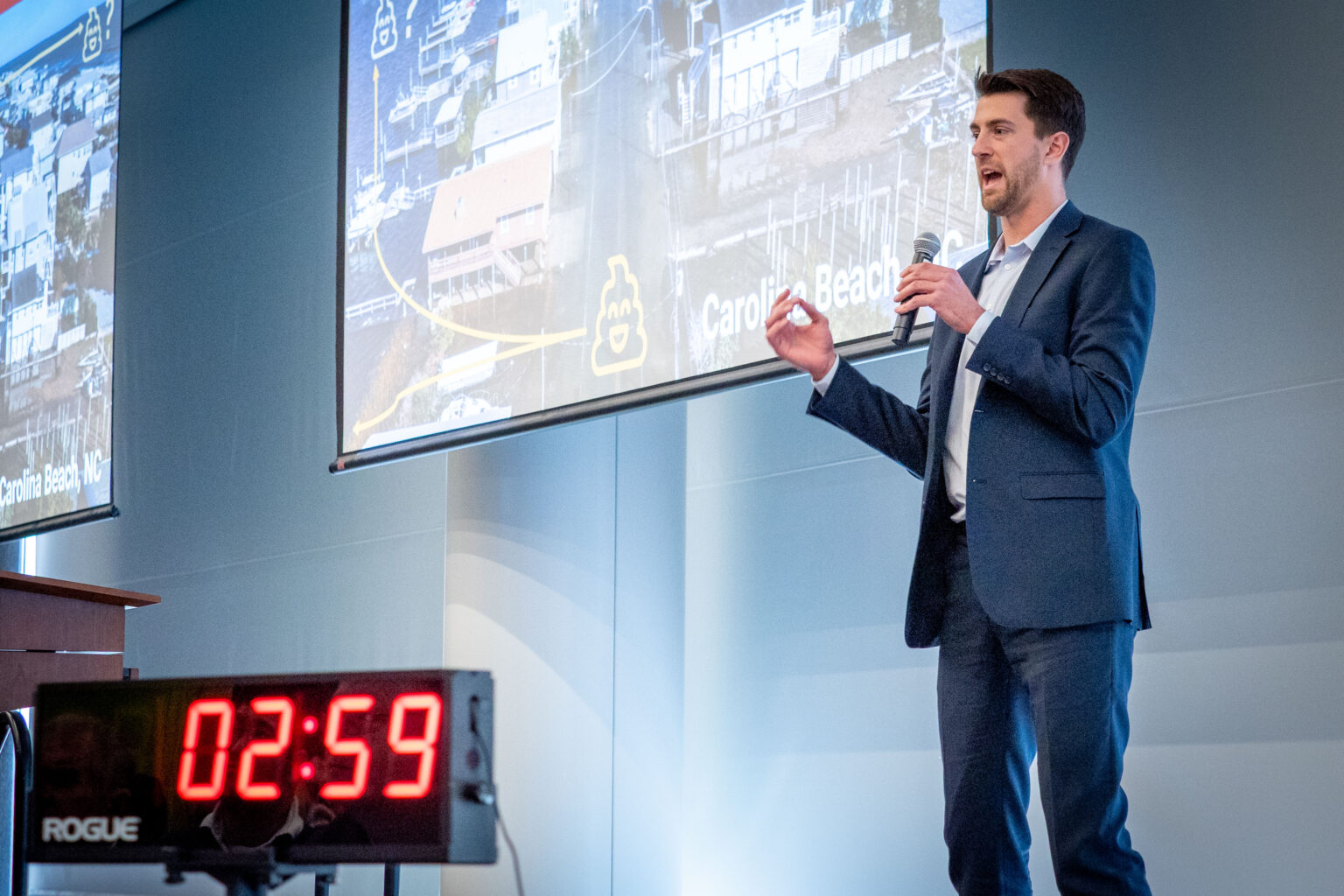 man holding a microphone speaks while standing next to a digital timer