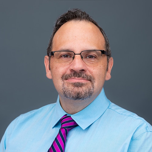 man with short dark hair, and goatee, wearing glasses, blue dress shirt and red/blue striped necktie